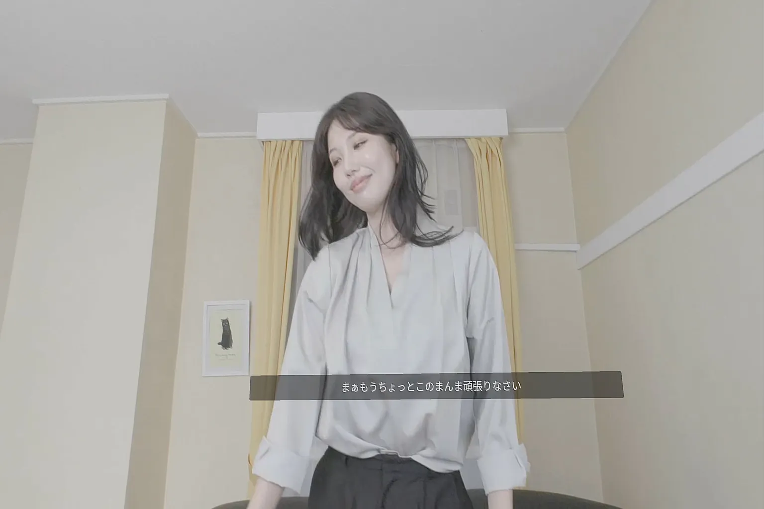 Video des japanischen JVR-Studios mit einer jungen, reifen Frau in einem Wohnzimmer. Japanische Untertitel zeigen ihre gesprochenen Dialoge.