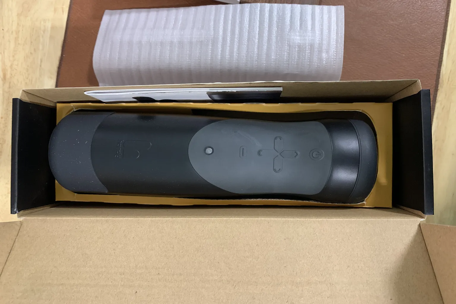 The unboxing scene after opening the package, with The Handy unit placed inside, showing the button layout and device design.